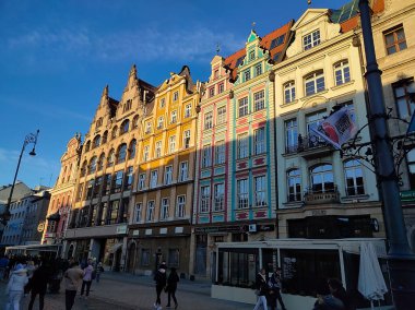 Wroclaw, Polonya - 17 Nisan 2022: Polonya 'daki Wroclaw Meydanı' nın merkezinde saatle eski belediye binasının yakınına giden insanlar