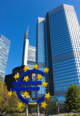 Frankfurt, Germany - April 20, 2022: Euro sign sculpture in a park among modern office towers in Frankfurt and Ukrainian flag- Ukraine and Europe concept