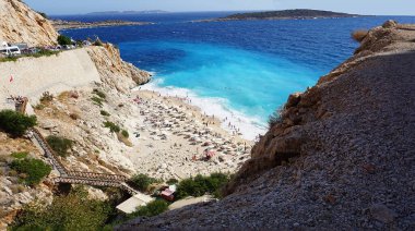 Sahilde dinlenen kalabalığın yol manzarası. Denizde yüzen insanlar. Türkiye 'de Kas ile Kalkan arasındaki Kaputas Plajı' nın üst manzarası