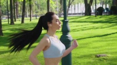 Spor tişörtlü fit bir kadın parkta koşuyor.