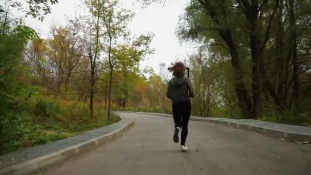 慢动作适合女运动员穿着运动服在路上跑着 路边是黄色的树 地上是落叶 在秋季拍摄了一些积极参加体育运动的人的照片之后 健康的概念 — 图库视频影像
