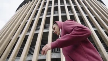 Modern binada ağır çekimde koşan kapüşonlu bir adam. Düşük açılı izleme çekimi sabah şehir ortamında koşucunun egzersiz yaparken. Sağlıklı yaşam tarzı kavramı