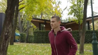 Spor giyimli formalı bir adam, sonbahar günü parkta ağır çekimde koşuyor, yaprakları yere düşmüş. İz sürme koşucusu antrenman sırasında zor nefes alıyor. Spor anlayışı