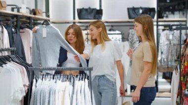 Genç kadınlar mağazadaki kıyafetlerle koridorda dikiliyorlar. El bilgisayarı en iyi arkadaşlar birlikte alışveriş yapar, süveter seçer, denerler. Moda kavramı