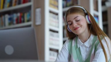 Öğrenci kütüphanede kulaklıklarla oturuyor, ödev yapıyor ve müzik dinliyor, ritme ayak uyduruyor, dizüstü bilgisayarı ön planda. Elde tutulan genç bir kadın melodiyi seviyor. Eğitim kavramı
