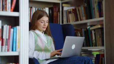Kitaplıklar ve dizüstü bilgisayarlar arasında koltukta oturan bir öğrenci. Kütüphanede okumak için interneti karıştıran genç bir kadının izini sürüyorum. Eğitim kavramı