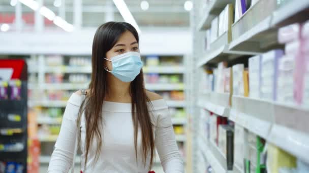 Asian woman in mask taking box from shelf at store