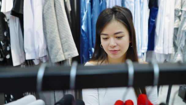 Mujer asiática eligiendo ropa en perchas en la tienda — Vídeos de Stock