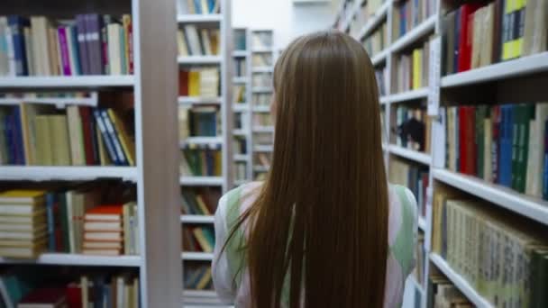 Mujer caminando en la biblioteca entre librerías — Vídeos de Stock