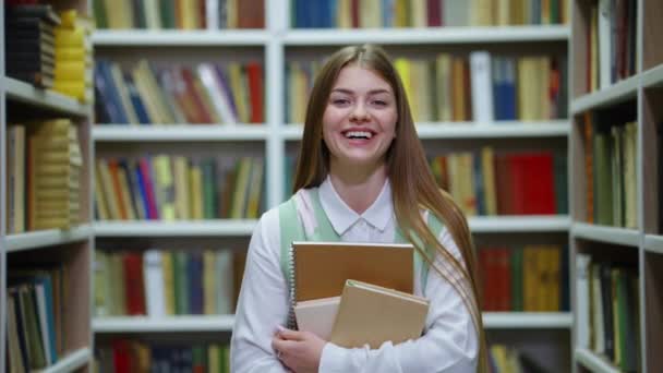 Студент держит книги и смеется в библиотеке — стоковое видео