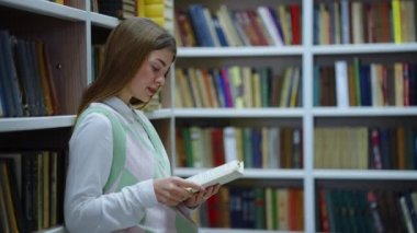 Kitaplığa yaslanan ve kitap okuyan bir kadın