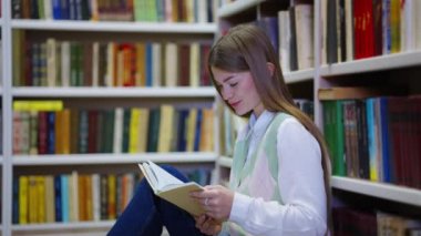 Kadın kütüphanede komik kitaplar okuyor ve gülüyor.