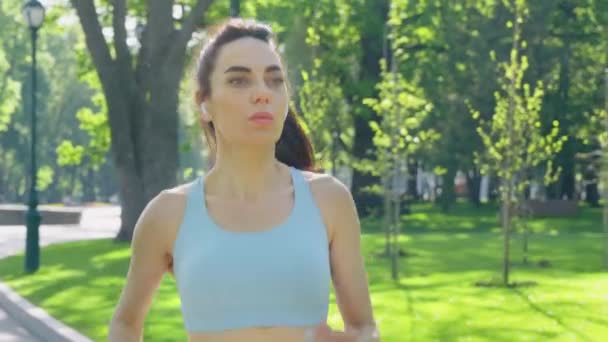 Mujer con auriculares corriendo en el soleado parque — Vídeos de Stock