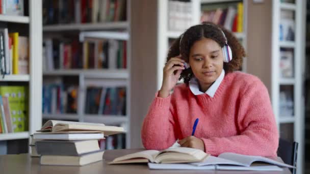 Афроамериканська студентка пише домашнє завдання і слухає музику. — стокове відео