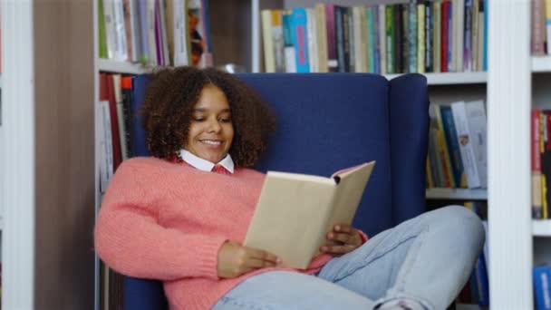 Chica negra leyendo libro en la biblioteca — Vídeo de stock