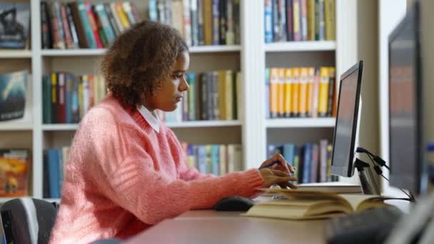 Zwart vrouwelijke student het doen van huiswerk in bibliotheek — Stockvideo