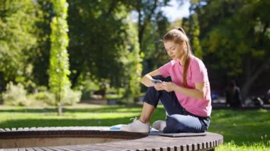 Kadın akıllı telefonu kontrol ediyor ve parkta gülüyor.