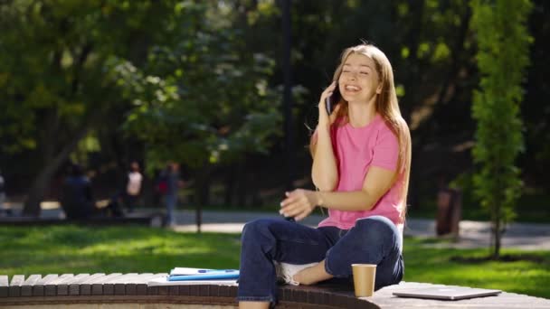 Женщина разговаривает по телефону и пьет кофе в парке — стоковое видео