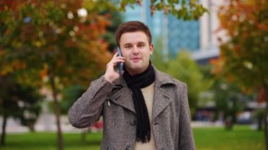 İş adamı parkta yürüyor ve telefonla konuşuyor.