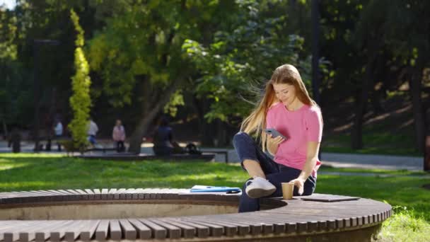 Mulher mensagens de texto no telefone e beber café no parque de verão — Vídeo de Stock