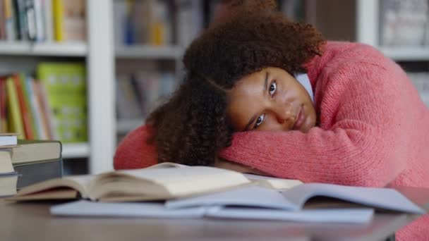 Schwarzes Mädchen liegt auf Büchern in Bibliothek — Stockvideo
