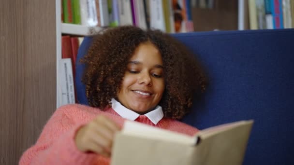 Svart tonåring läser bok i biblioteket — Stockvideo