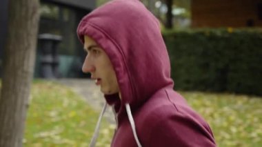 Kapüşonlu bir adam sonbaharda parkta koşuyor.