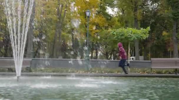 Slow motion jogger running behind fountains in park — Stock Video
