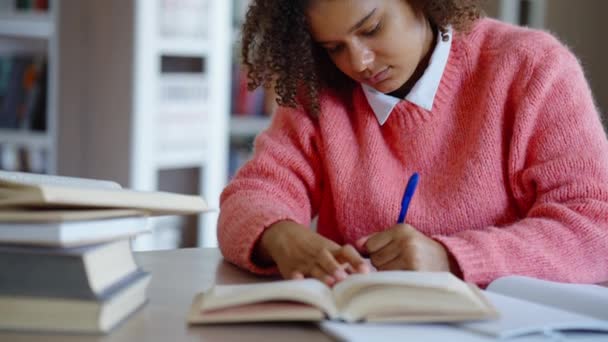 Estudiante afroamericana haciendo deberes en la biblioteca — Vídeos de Stock