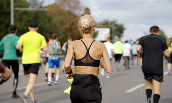 Blonde woman with hair bun running marathon on city road — Stock Photo, Image