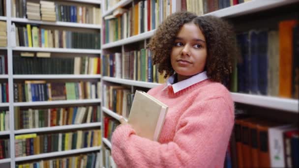 Zwart meisje leunen op boekenkast in bibliotheek — Stockvideo