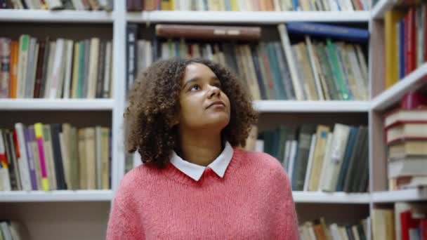 Чорна дівчина ходить в бібліотеці серед книжкових шаф — стокове відео