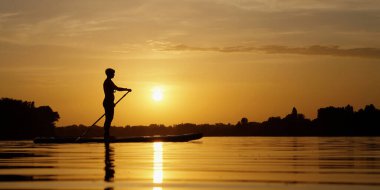 Sup panosunda kürek çeken bir kadın silueti.