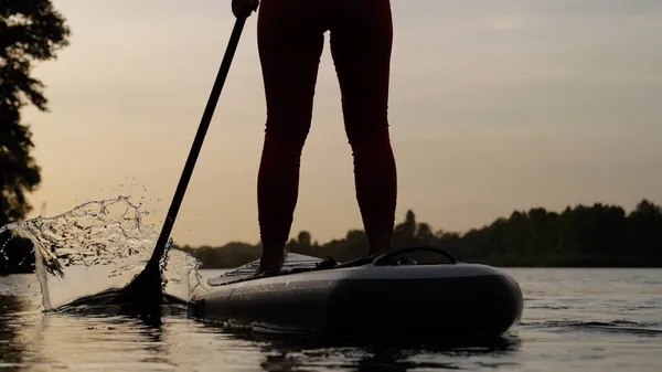 Gün batımında SUP panosunda kürek çeken bir kadın.