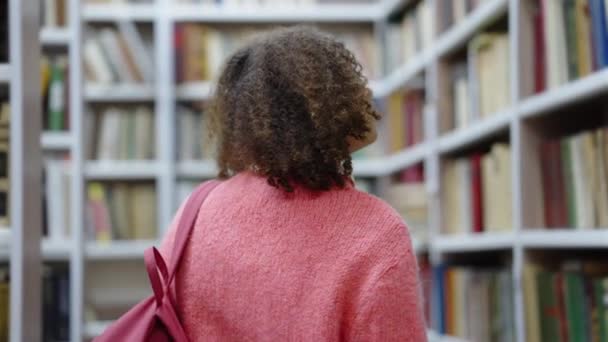 College student promenader bland bokhyllor i biblioteket — Stockvideo