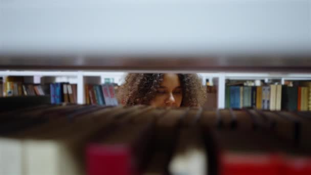 Menina negra atrás da estante na biblioteca — Vídeo de Stock