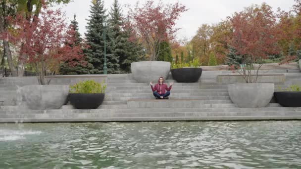 Йога розмірковує біля води в парку. — стокове відео