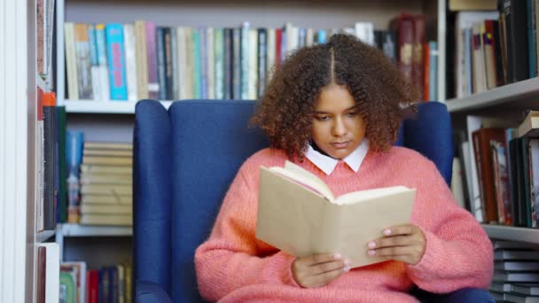 Svart flicka läser bok i biblioteket — Stockvideo