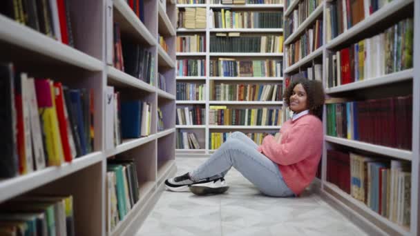 Svart tonåring flicka sitter i biblioteket — Stockvideo