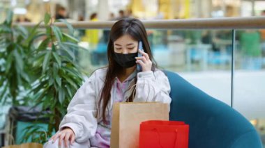 Maskeli bir kadın alışveriş merkezinde telefonla konuşuyor.