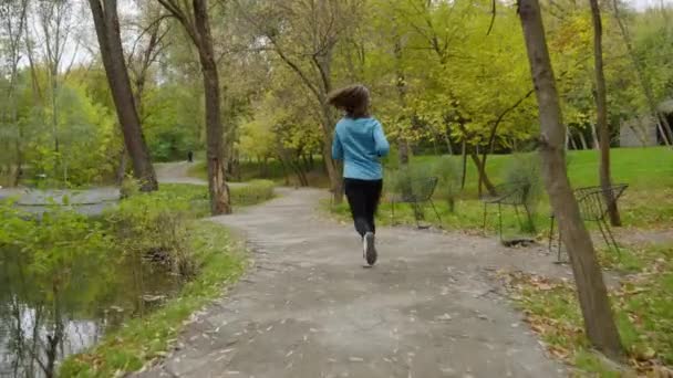 Жінка біжить біля ставка в парку в повільному русі — стокове відео
