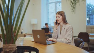 İş kadını laptopta çalışıyor ve kafede telefonla konuşuyor.