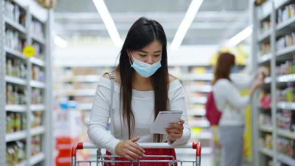Pelanggan Asia bertopeng dengan daftar belanja di toko — Stok Video