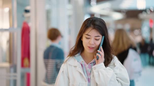 Jonge vrouw wandelen in het winkelcentrum en praten over de telefoon — Stockvideo