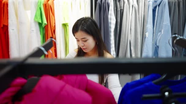 Asijská žena výběr bunda v módním obchodě — Stock video