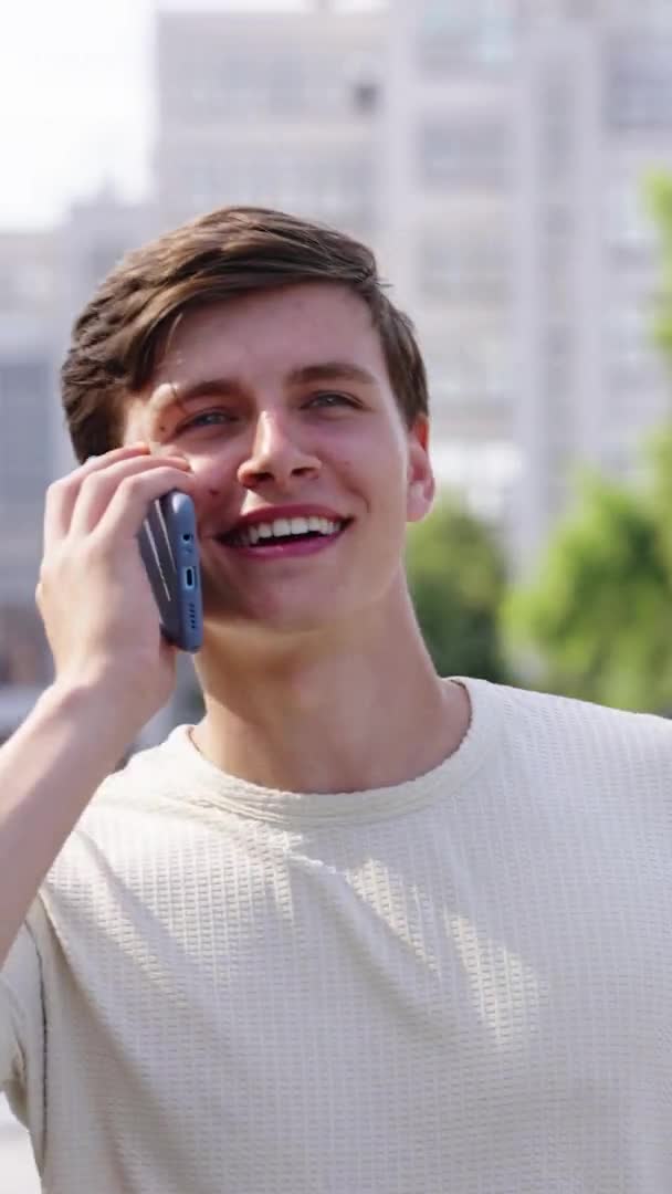 Dikey Ekran: Gülümseyen adam şehirde yürürken telefonla konuşuyor — Stok video