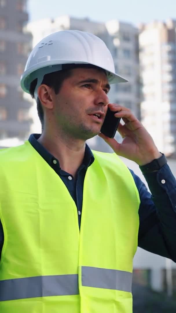Tela vertical: Empreiteiro de construção falando por telefone contra o novo distrito da cidade — Vídeo de Stock