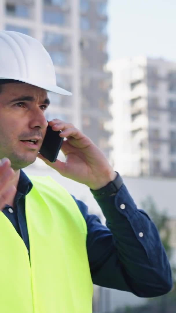 Écran vertical : Ingénieur parlant au téléphone sur le chantier de construction — Video