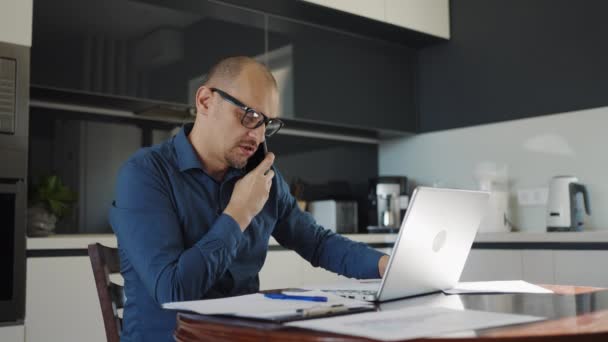 Επιχειρηματίας μιλάει στο τηλέφωνο εργασίας από το σπίτι κάθεται στην κουζίνα — Αρχείο Βίντεο