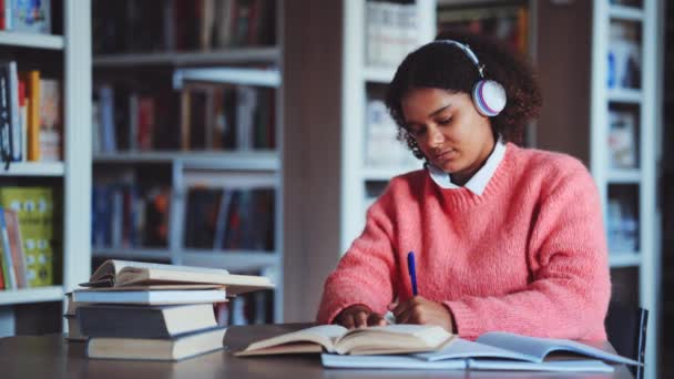 Chica afroamericana haciendo deberes en la biblioteca — Vídeo de stock